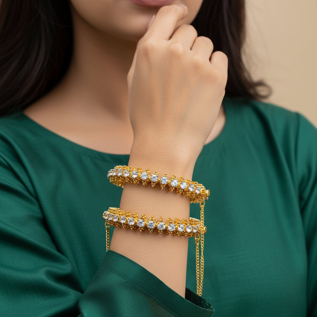 Two 24K gold plated diamond-cut bangle bracelets with real American zircons, featuring openable clip locks and kara styling, displayed on a rocky surface.